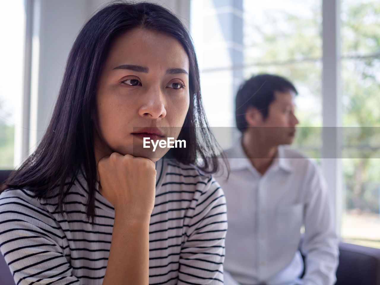 PORTRAIT OF A YOUNG WOMAN LOOKING AWAY WHILE STANDING AGAINST WINDOW