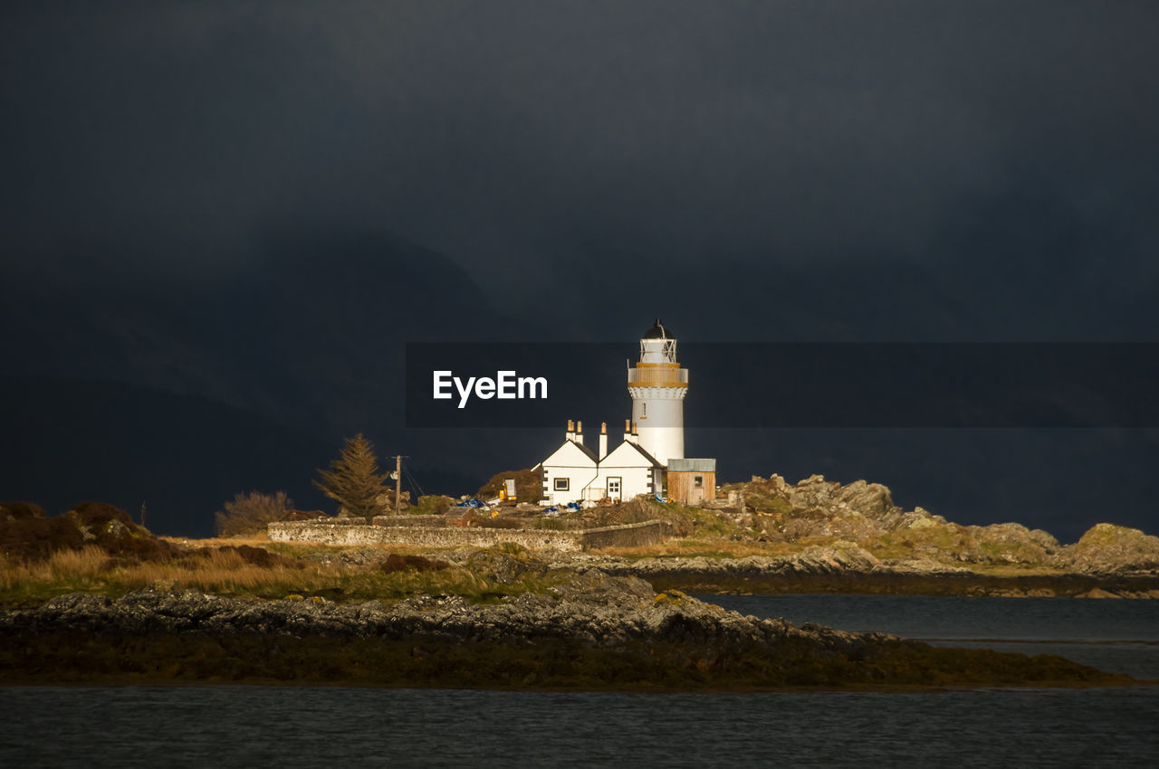 Lighthouse amidst sea and buildings against sky