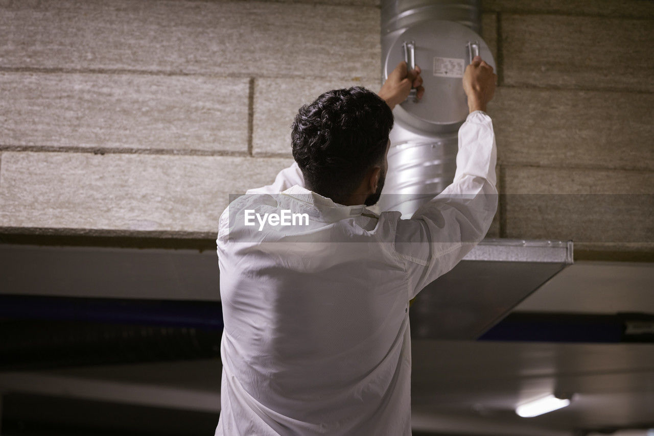 Rear view of man checking air duct