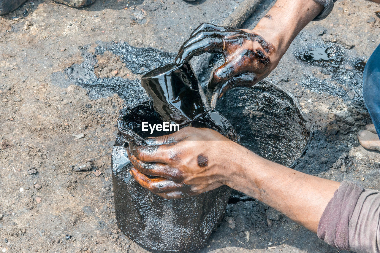 Low section of worker filling tar in container