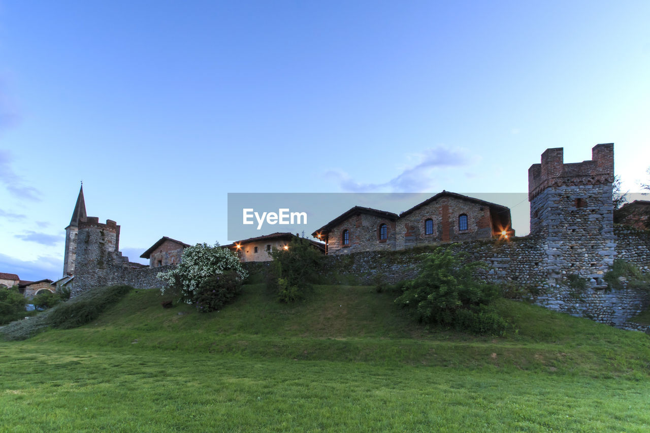 HOUSES ON GRASSY FIELD AGAINST SKY