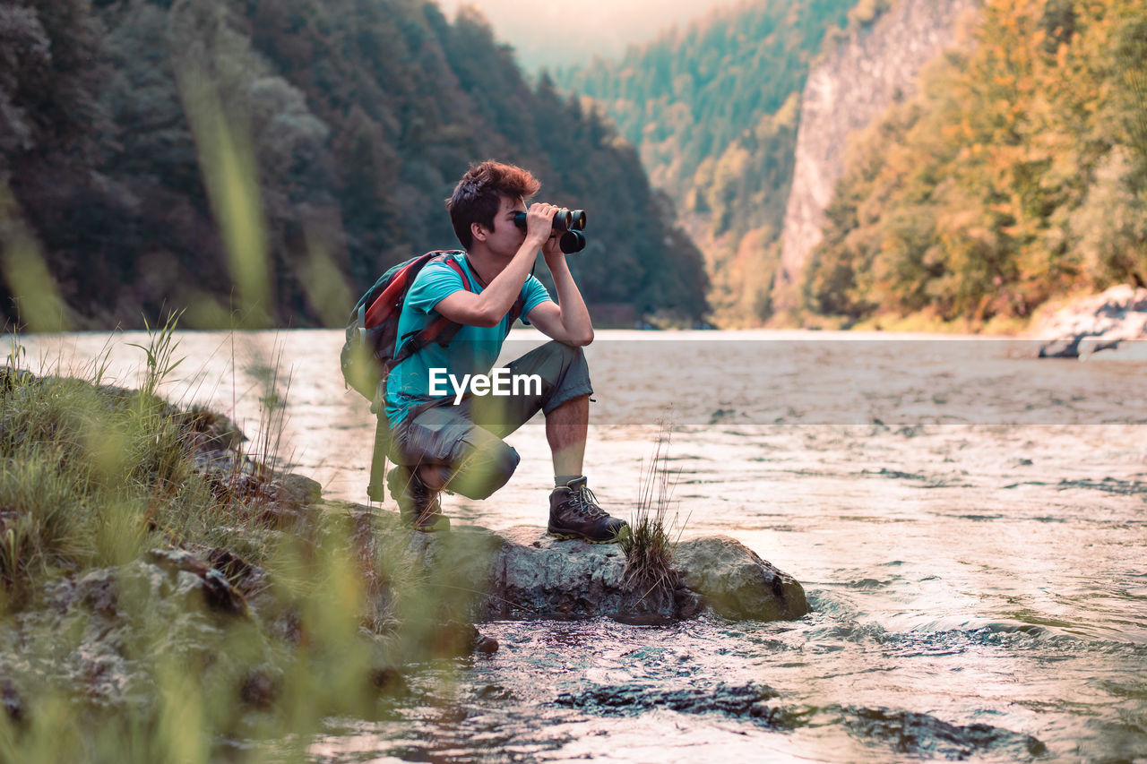 Boy with water bottle crouching at riverbank