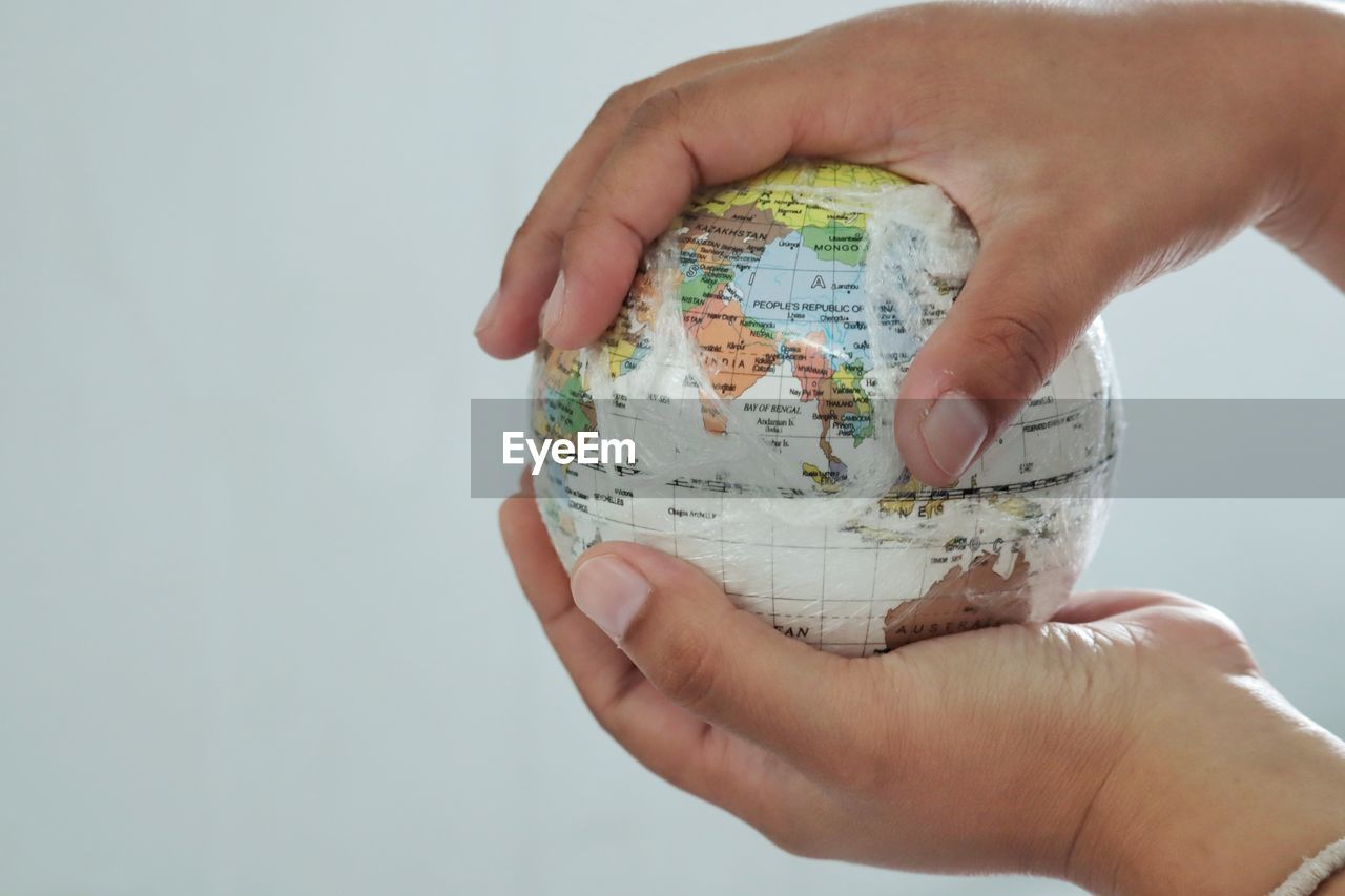 Cropped hands holding globe against white background