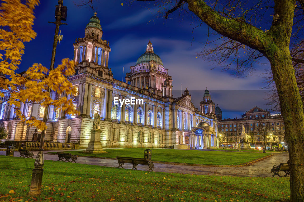 The beautiful city hall of belfast illuminated at twilight with some autumnal trees