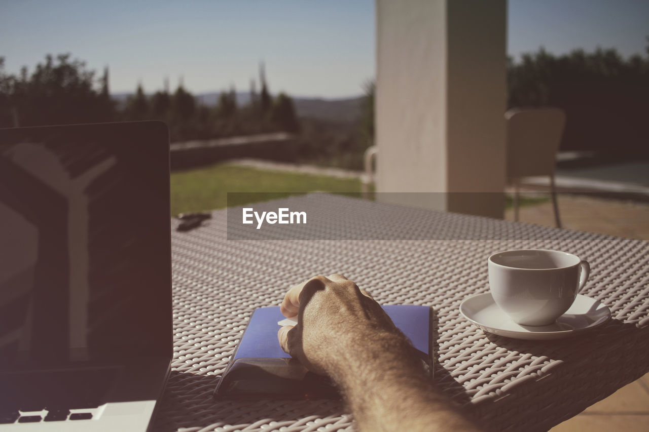 Cropped hand using wireless mouse by coffee cup on table