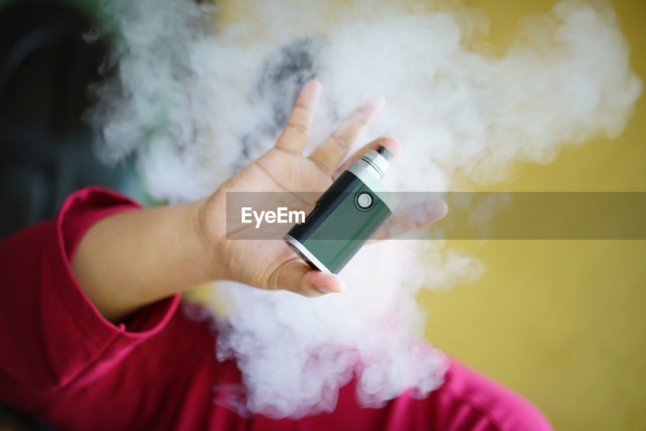 Close-up of man holding electronic cigarette amidst smoke