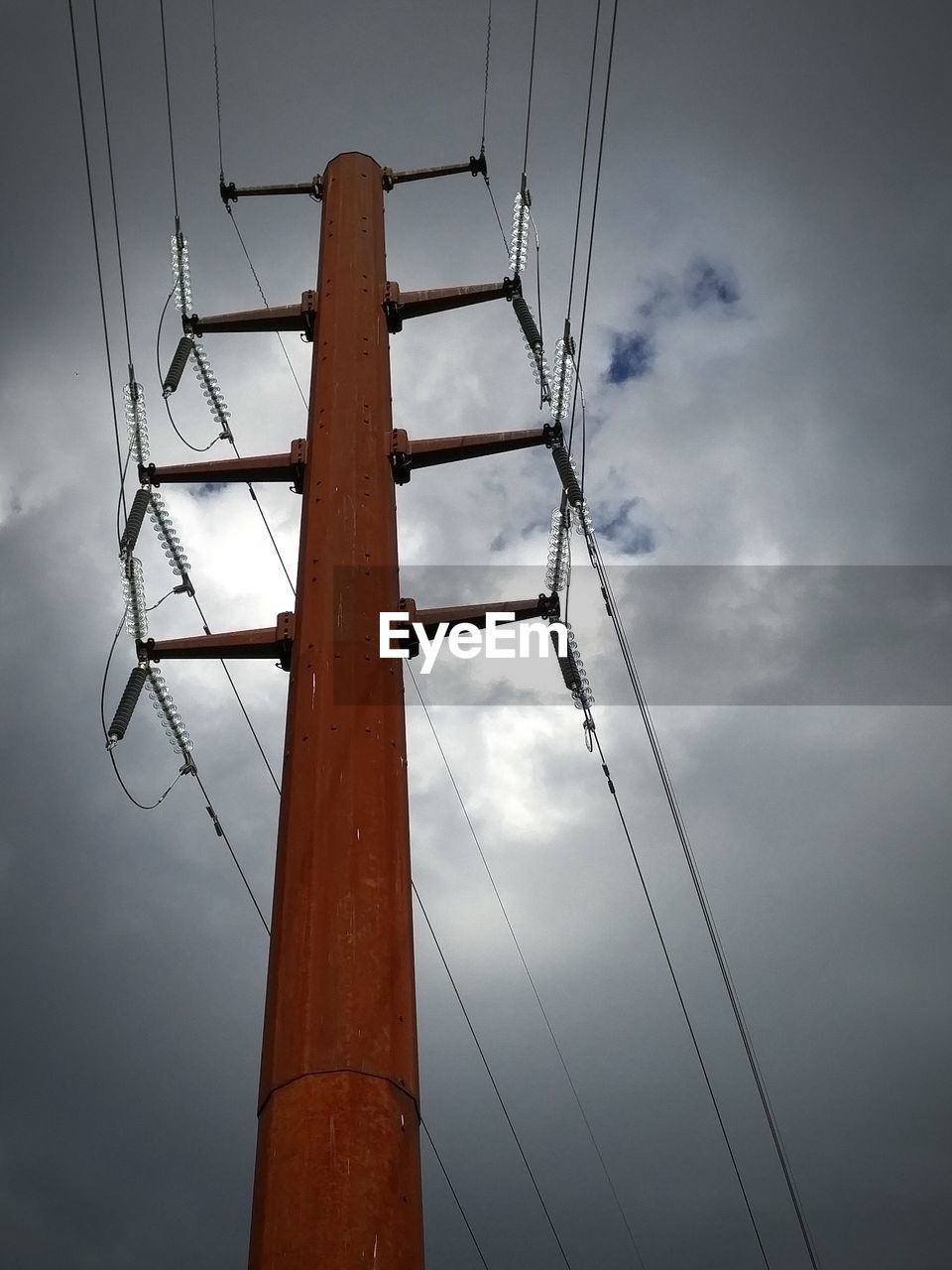 Low angle view of electricity pylon against cloudy sky