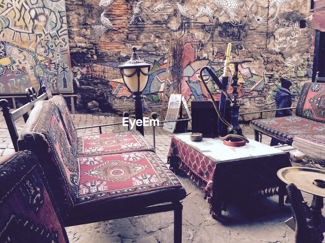 Hookah on table by empty chairs against graffiti on wall