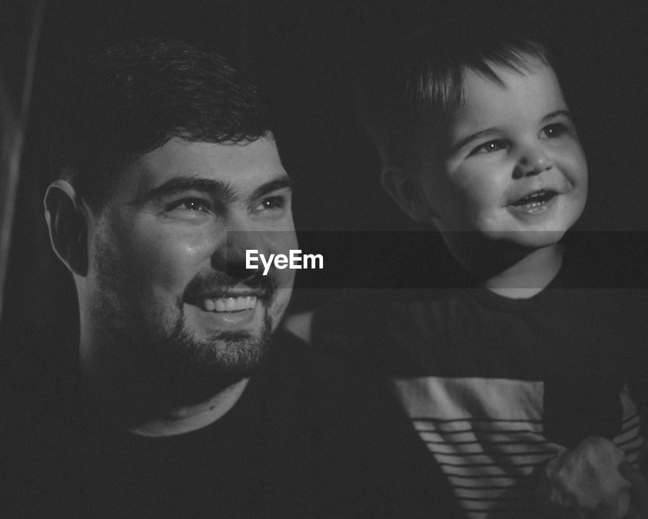 Smiling father and son looking away against black background