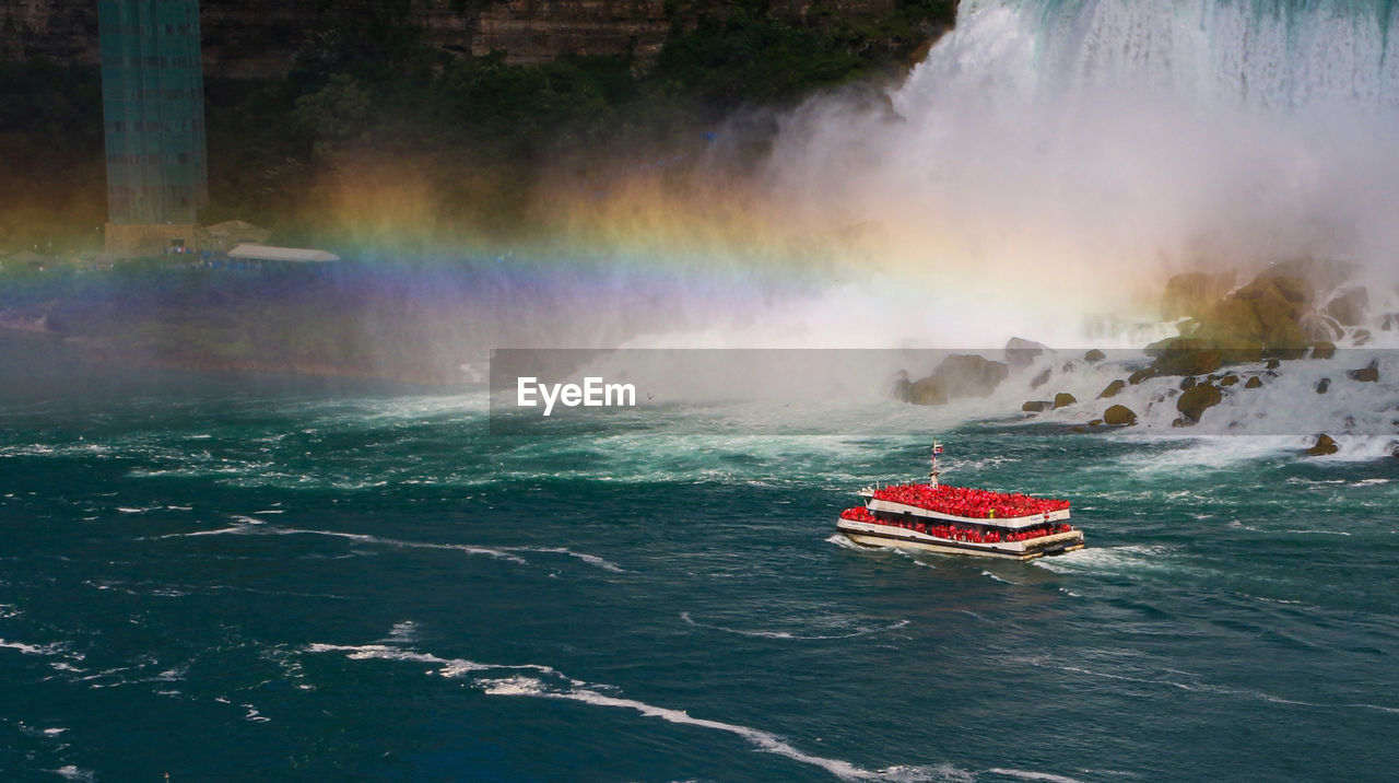 The hornblower boat traveling under a rainbow in front of the american falls of niagara falls.