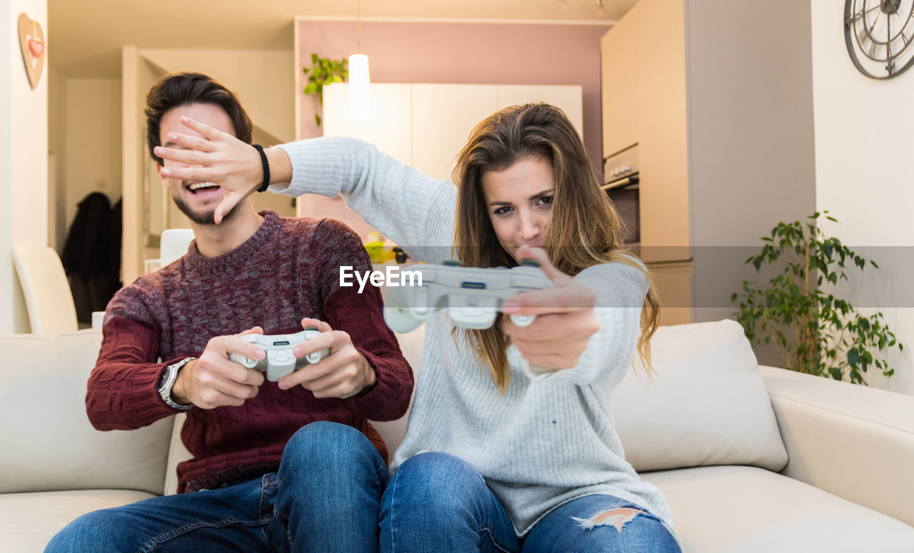 Woman covering man face while playing video game at home