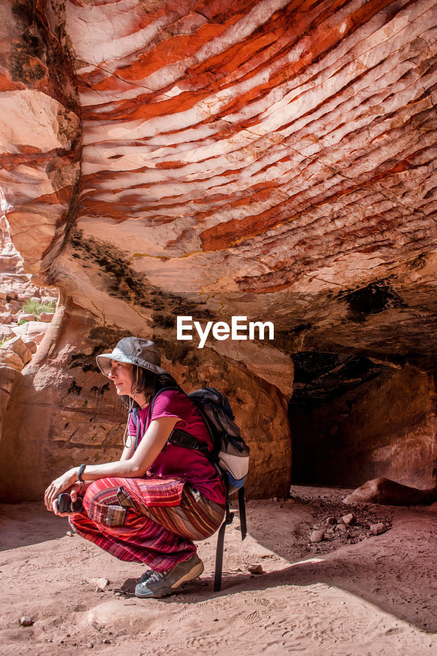 SIDE VIEW OF WOMAN SITTING ON ROCK AT MOUNTAIN