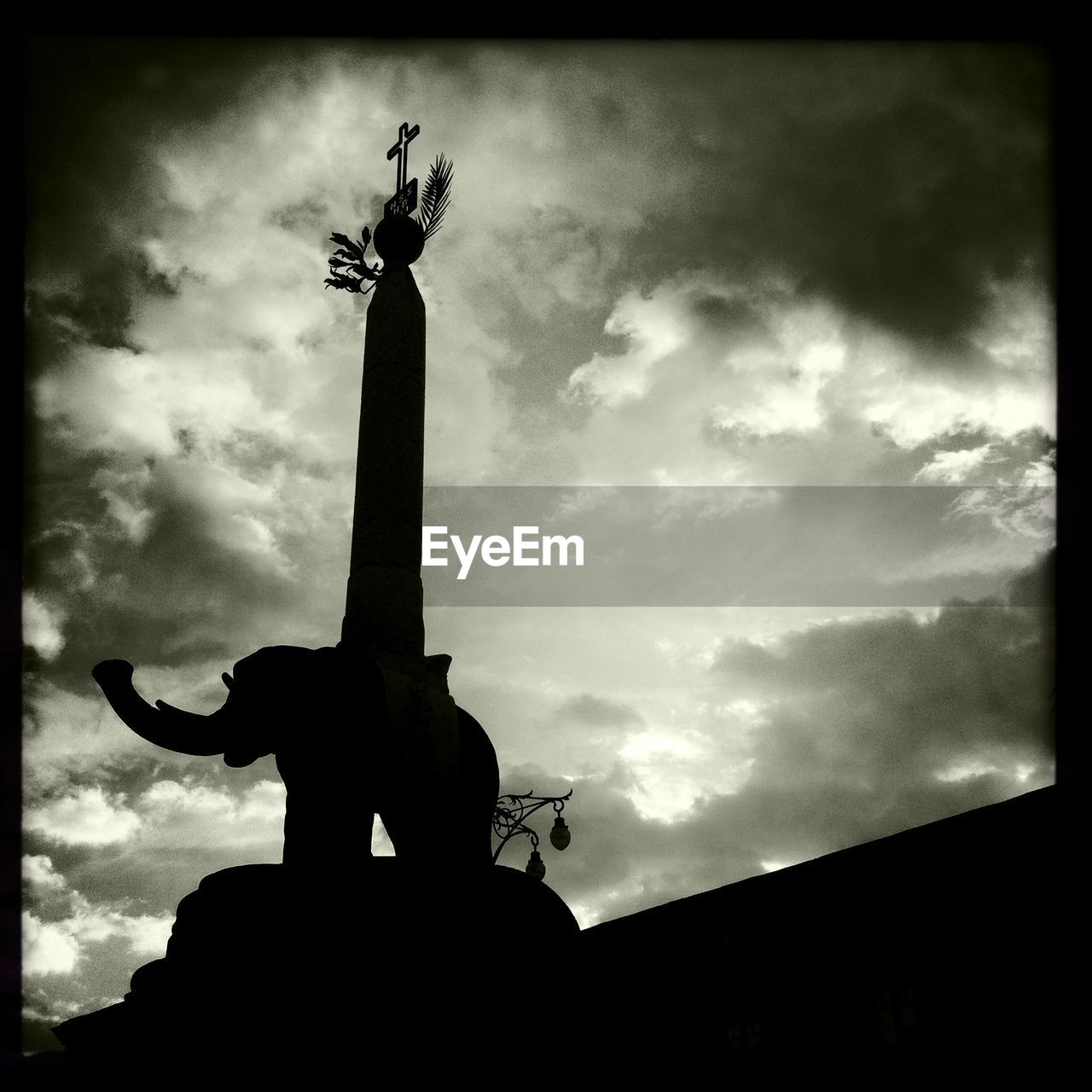 Low angle shot of cross and animal statue against cloudy sky