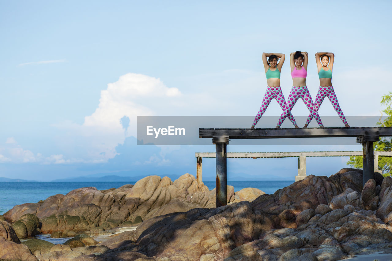 Portrait of three women exercising on pier at beach 