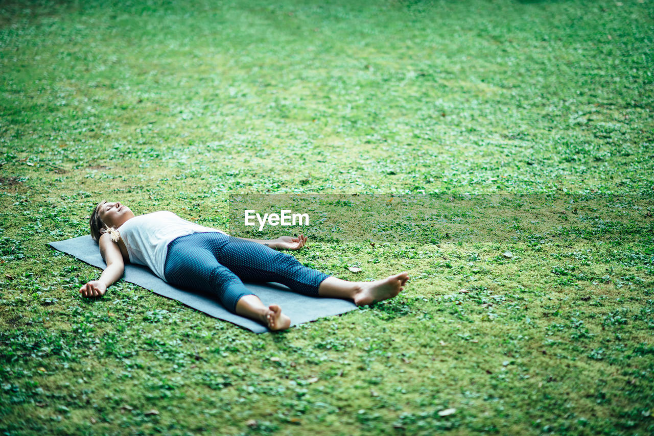 Young woman practicing shavasana in park