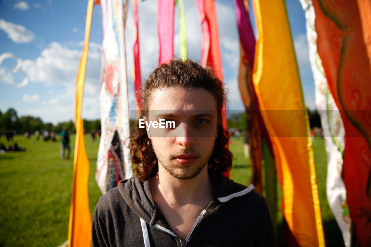 Portrait of young man standing by fabrics on park during sunny day