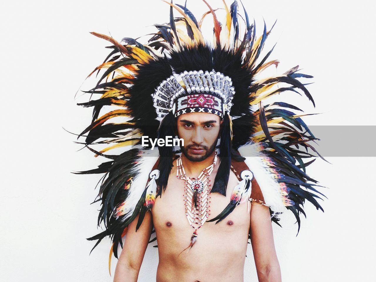 Portrait of young man wearing apache headdress against white background