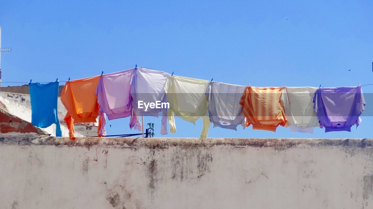Low angle view of multi colored clothesline hanging on building terrace against clear blue sky