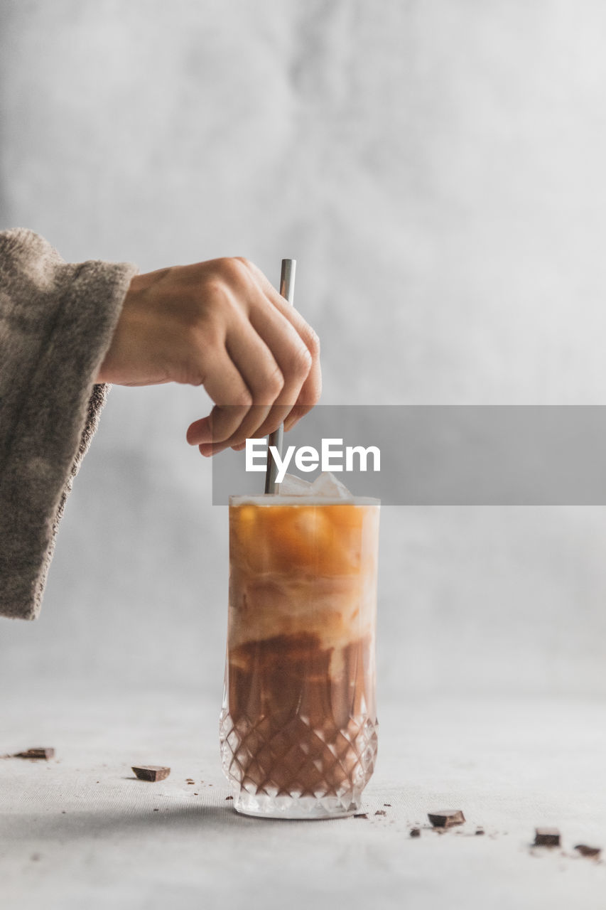 Midsection of person holding metal straw in iced coffee drink on table