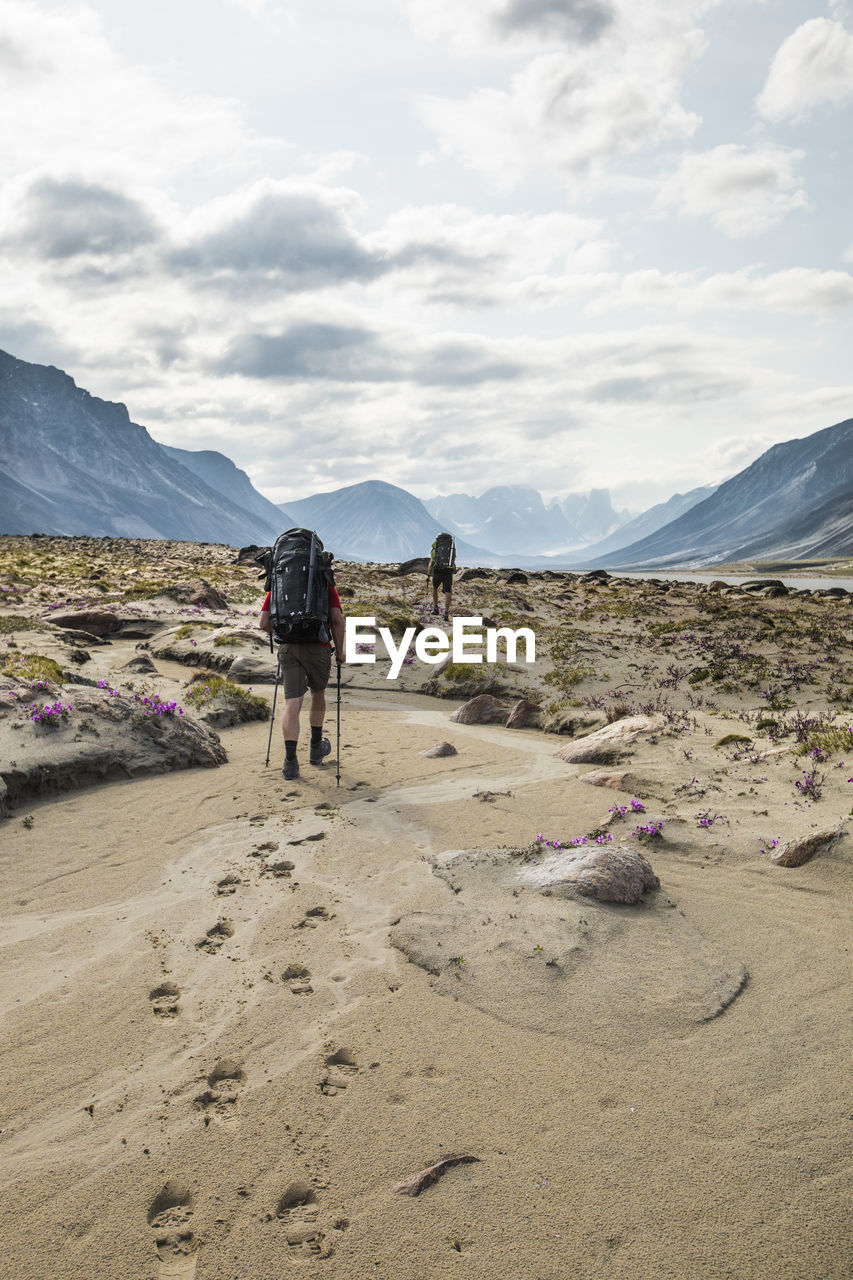 Rear view of two backpackers hiking, leaving footprints in the sand.