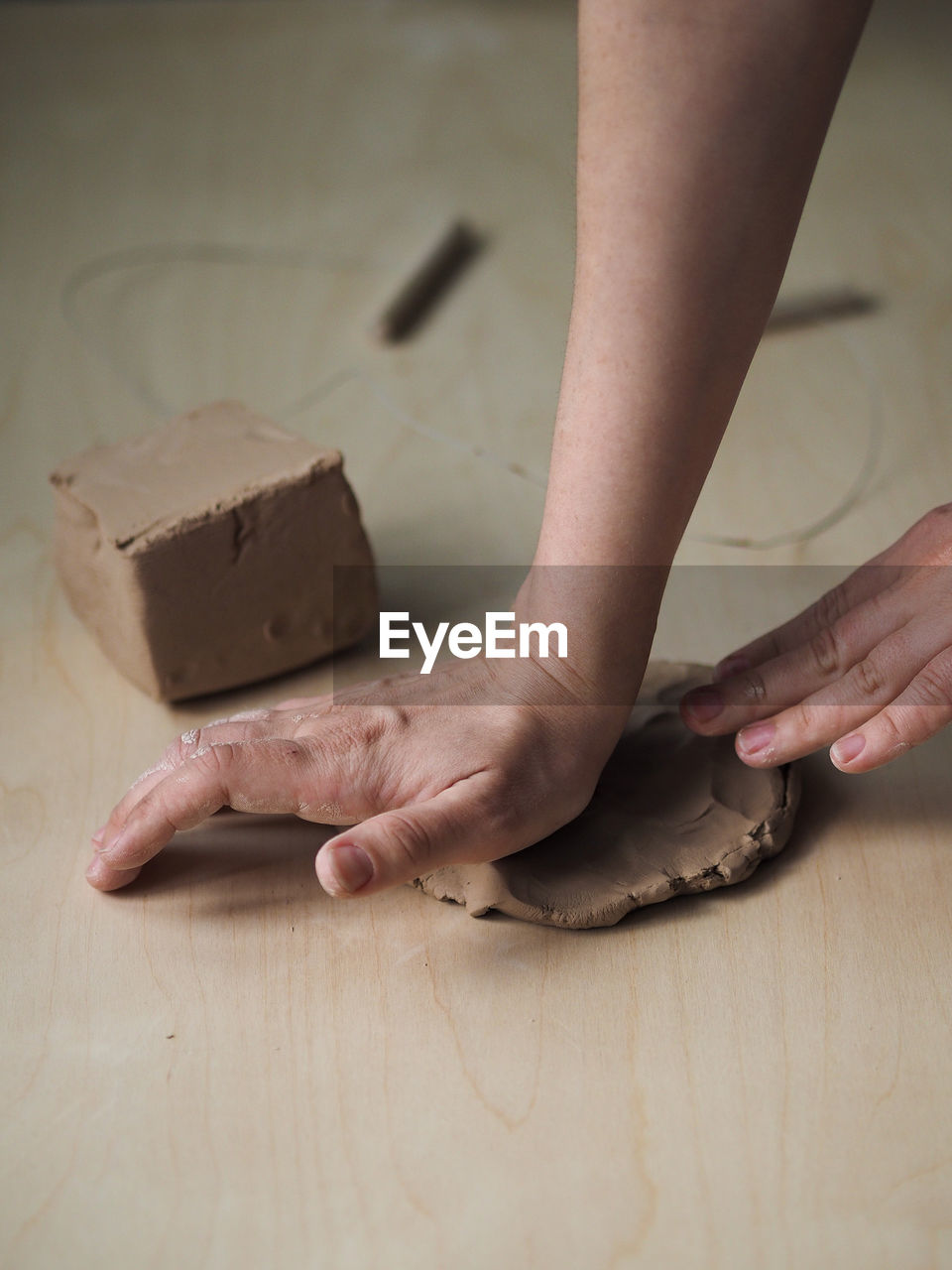 Young woman prepares clay to create a mug on a wooden table. 