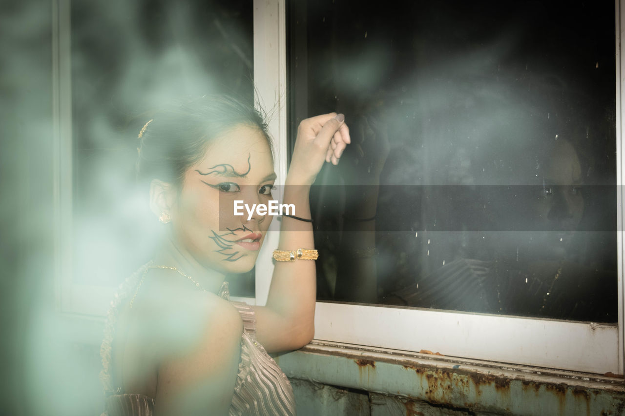 Portrait of woman with face paint standing by window