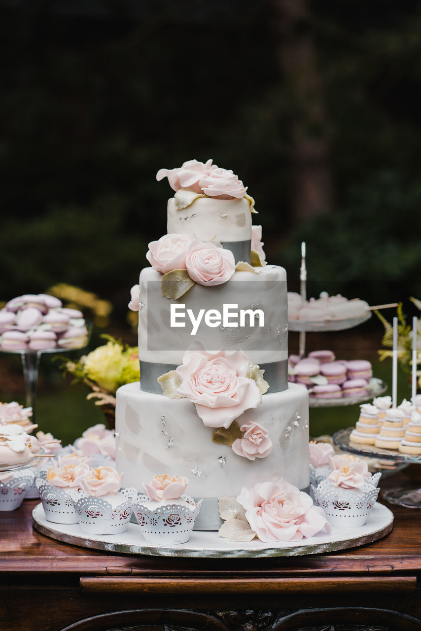Big luxury white wedding cake with pink roses and cupcake decoration on the candy bar table