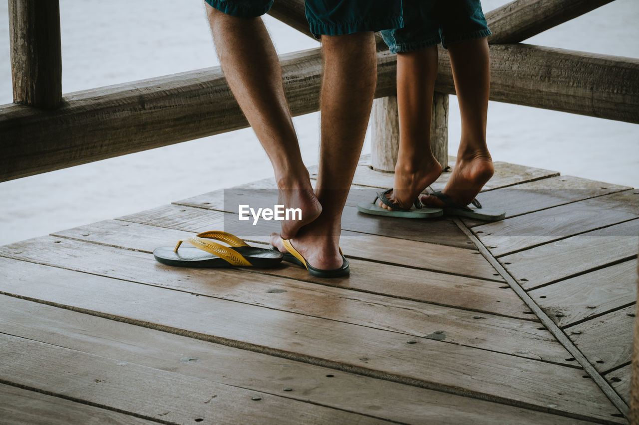 Low section of people wearing flip-flops on wooden floor