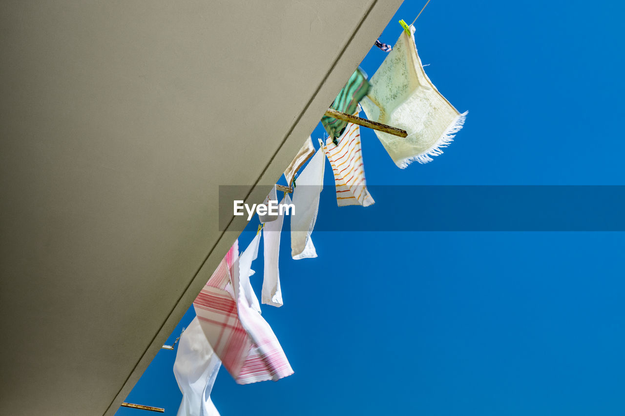 LOW ANGLE VIEW OF CLOTHES DRYING AGAINST BLUE SKY