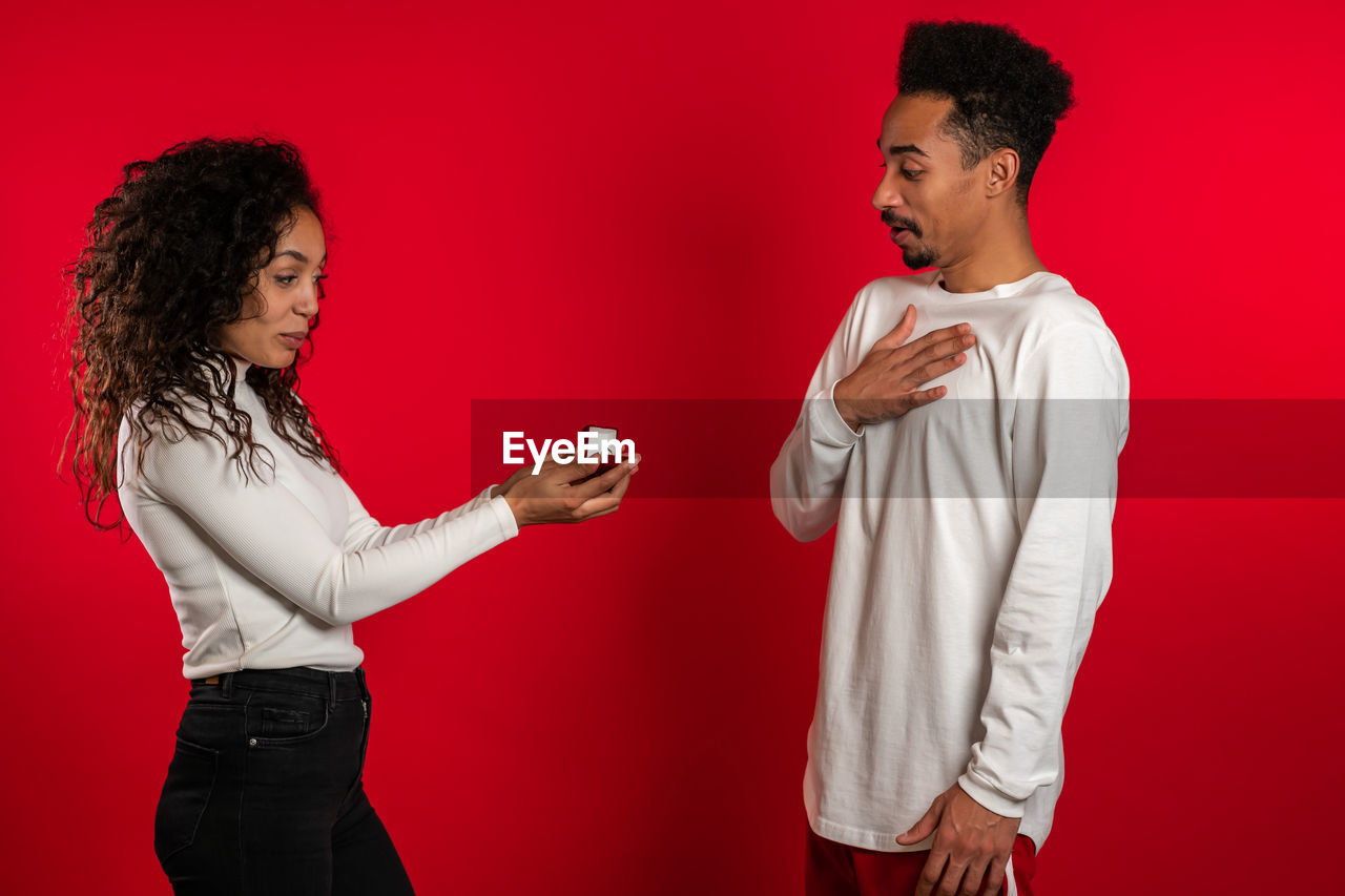 YOUNG MAN AND WOMAN AGAINST RED BACKGROUND