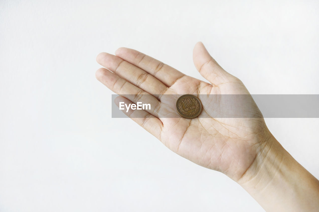 Close-up of woman hand holding coin against white background