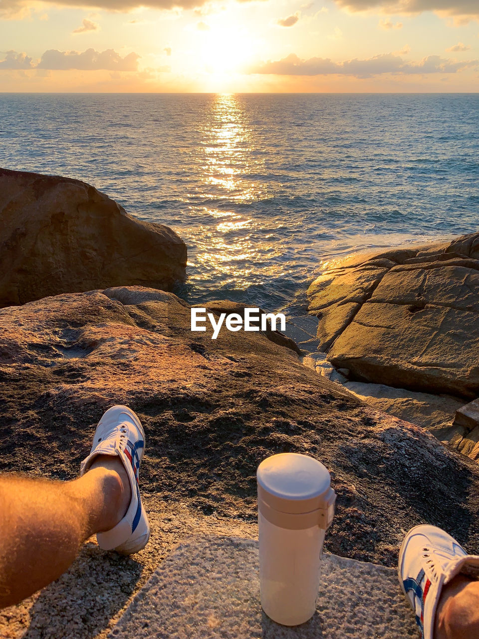 LOW SECTION OF PERSON ON SEA SHORE DURING SUNSET