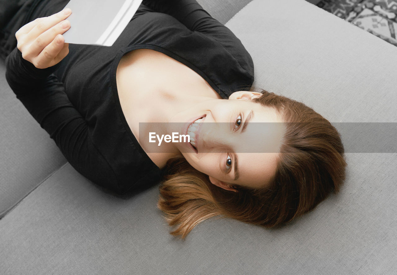 High angle portrait of woman reading book while lying on bed at home