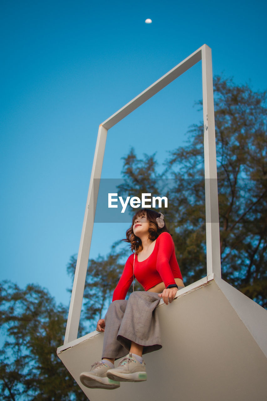 Low angle view of woman listening music against blue sky