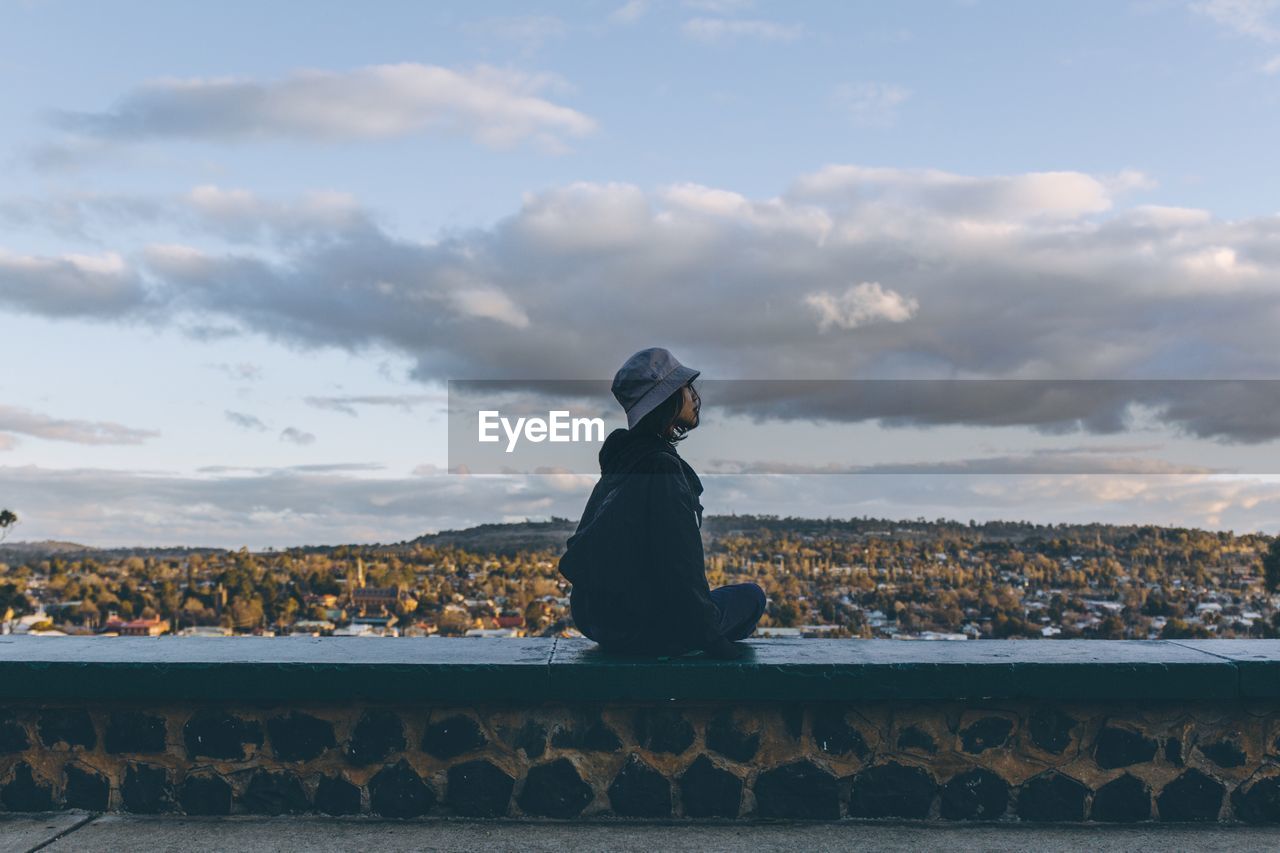 Woman sitting on wall against sky