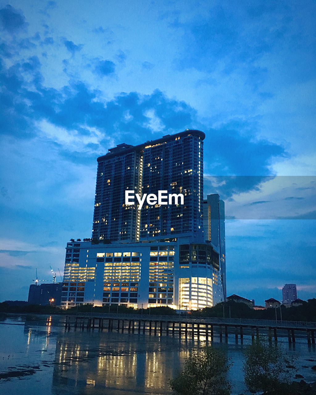 LOW ANGLE VIEW OF ILLUMINATED BUILDING BY RIVER AGAINST SKY