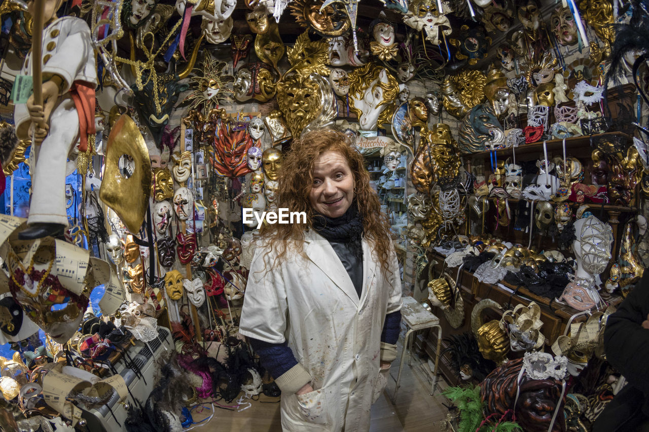 Portrait of woman smiling while standing amidst masks in store