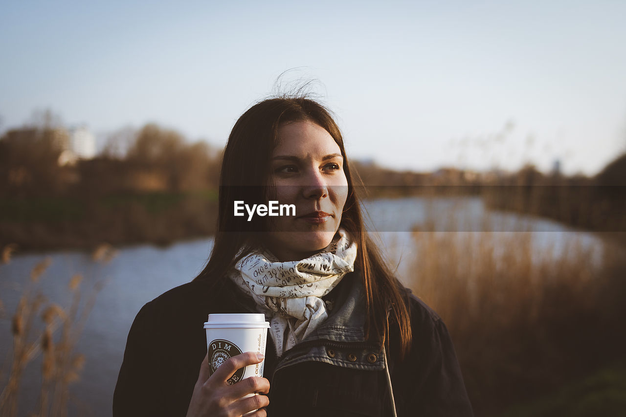 Young woman drinking water against sky