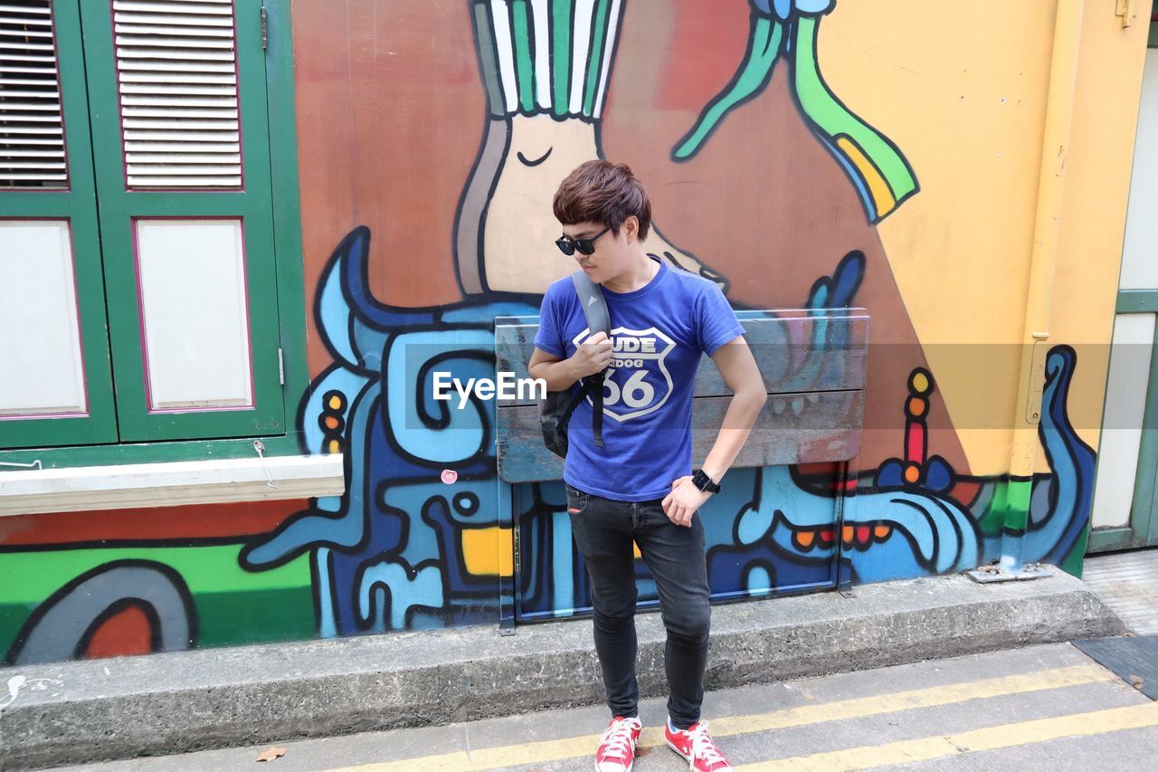 FULL LENGTH OF BOY STANDING BY GRAFFITI WALL