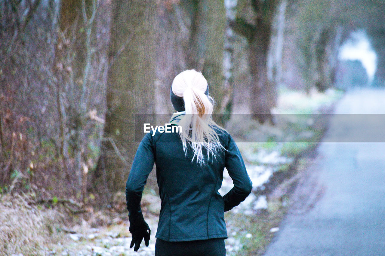 Rear view of woman jogging on road amidst trees