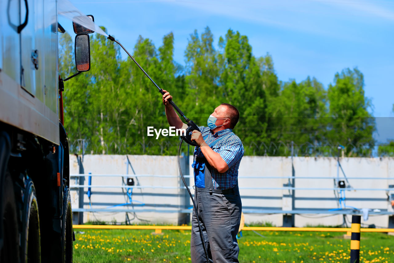 Side view of man wearing mask cleaning truck