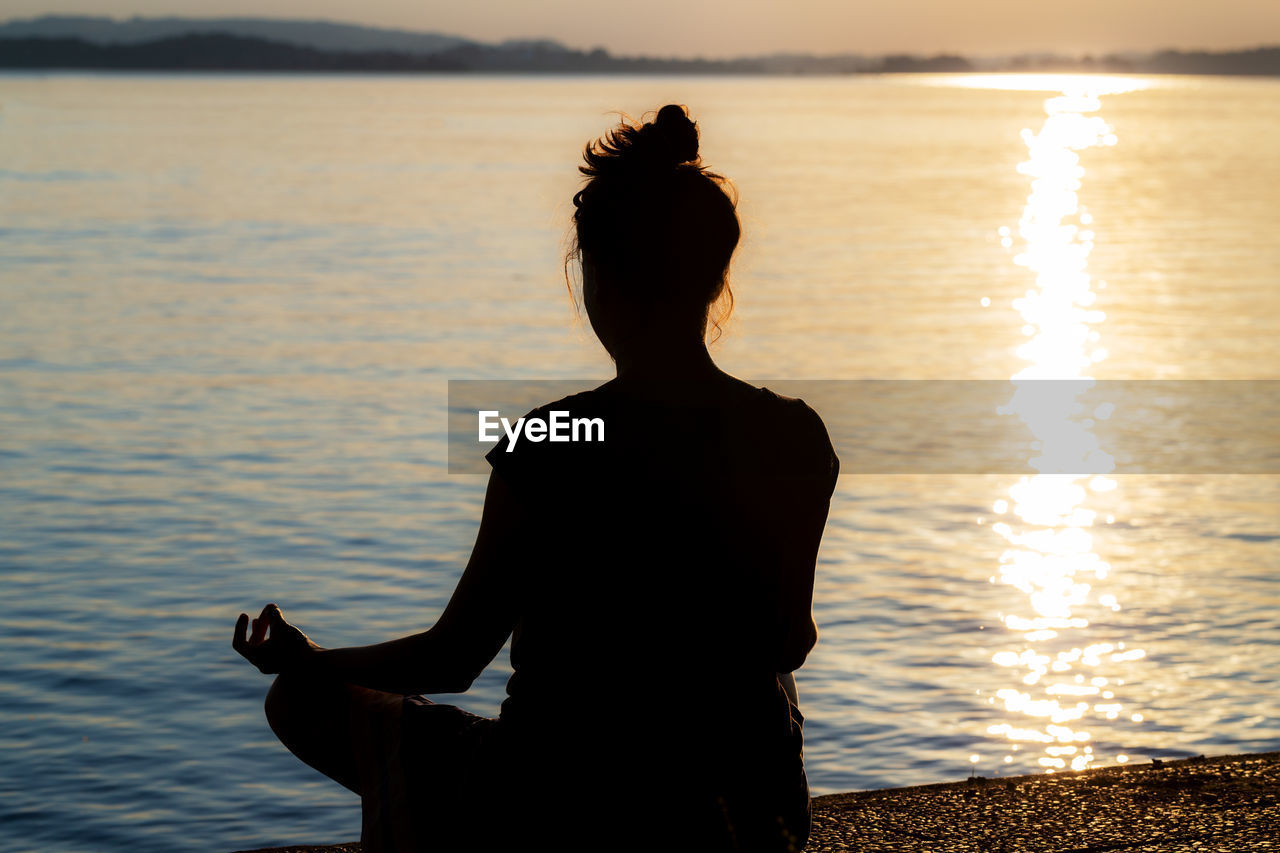 Woman doing yoga against sea during sunset