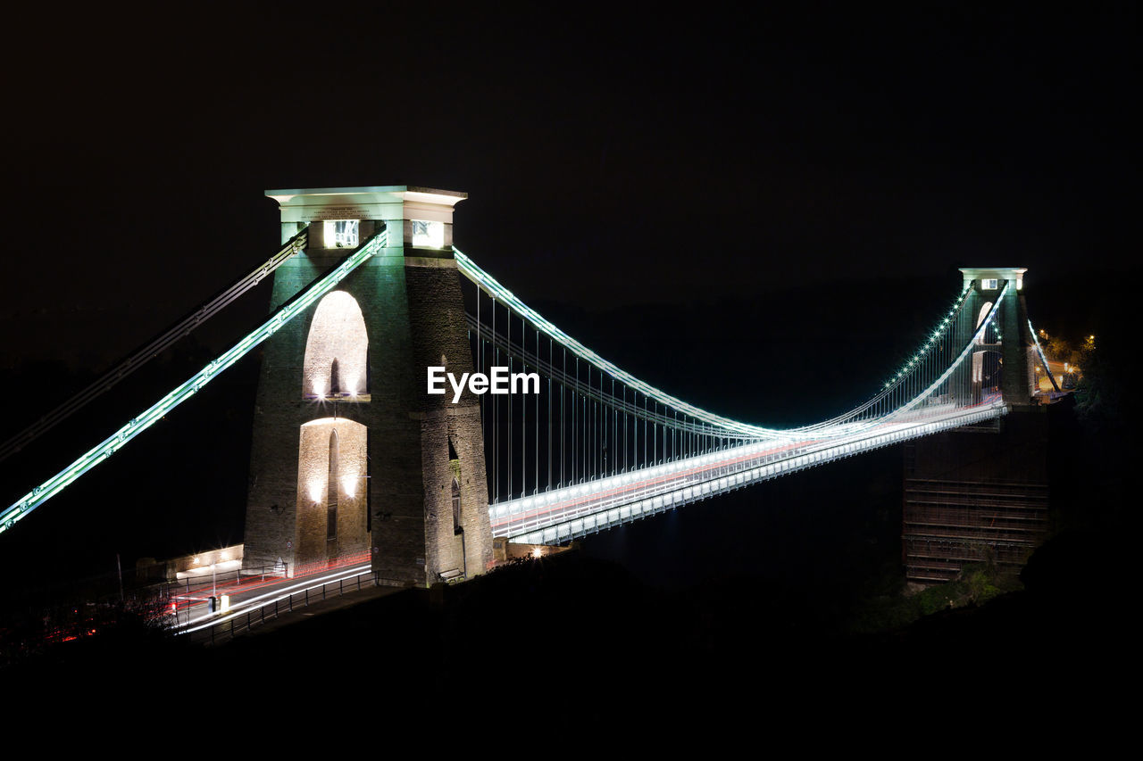 LOW ANGLE VIEW OF ILLUMINATED BRIDGE AT NIGHT