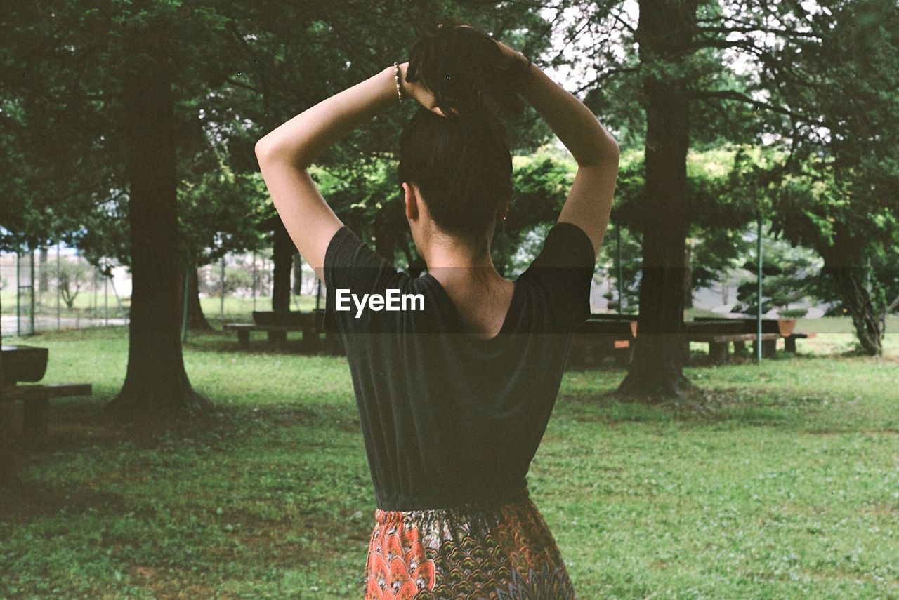 Rear view of woman tying hair on field