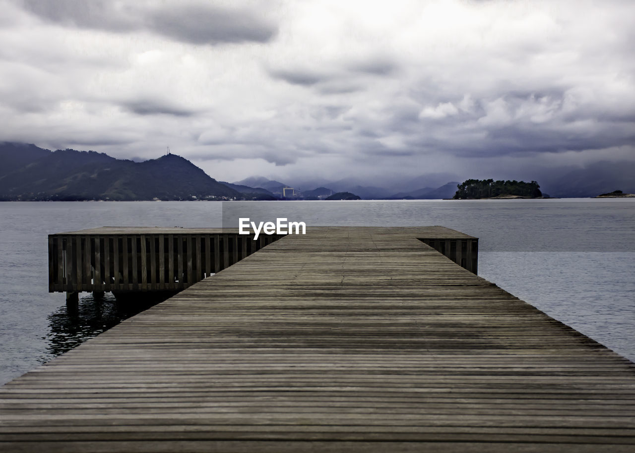 Pier over lake against cloudy sky