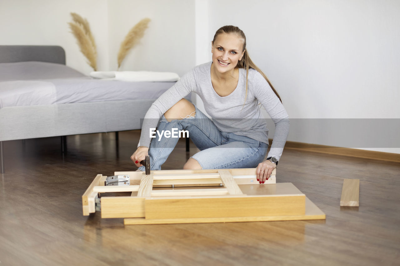 Happy woman collects furniture with a hammer in the bedroom