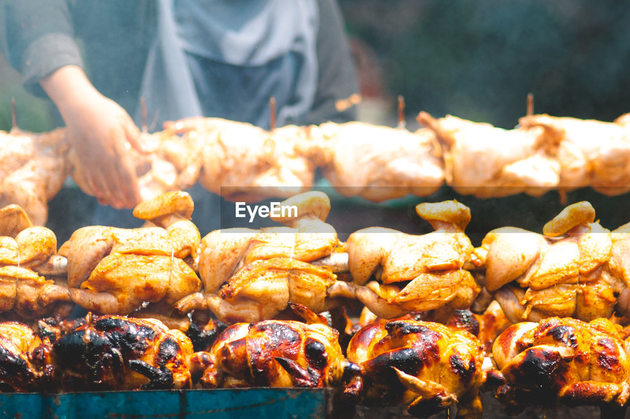Close-up of person roasting chicken at barbecue grill