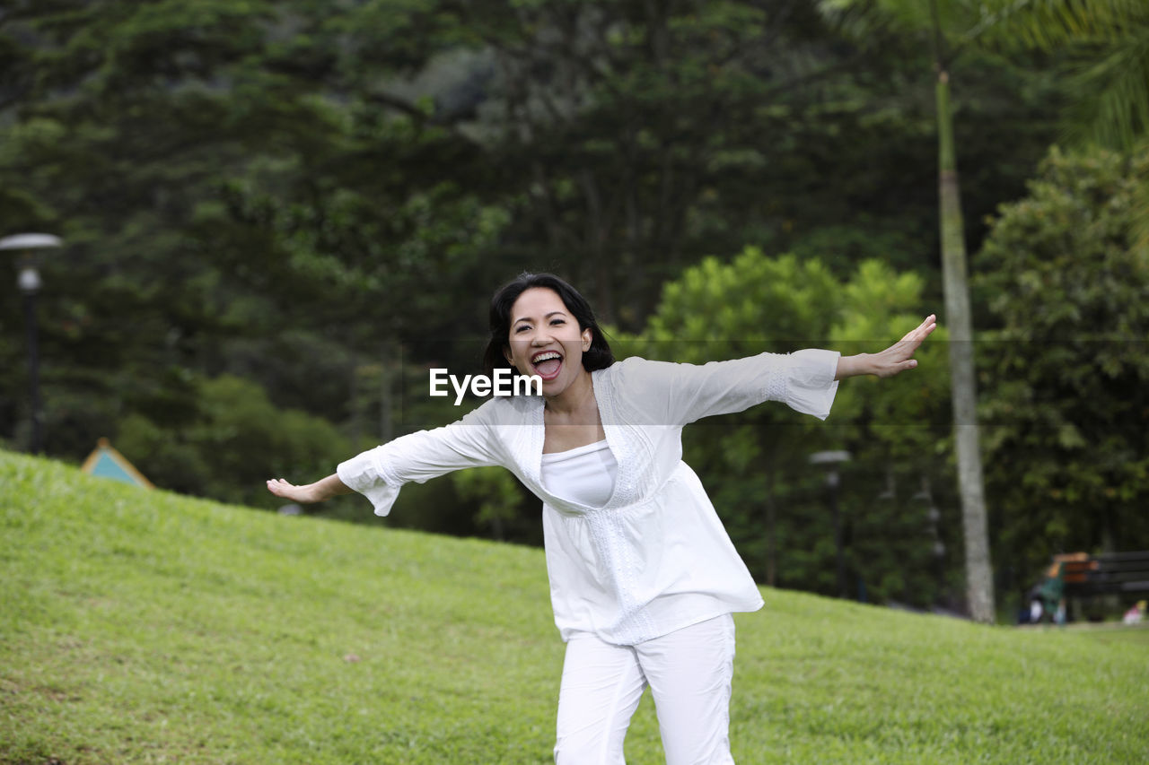 Portrait of happy woman with arms outstretched standing on field at park