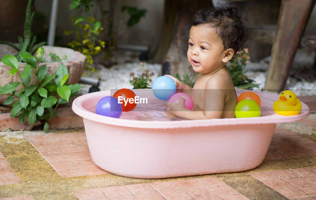 Shirtless baby boy playing with colorful balls in bathtub