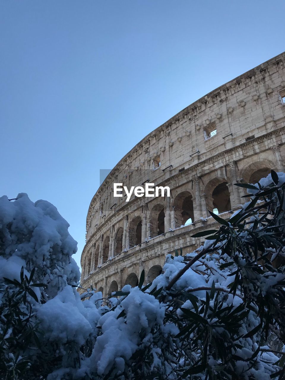 Low angle view of coliseum against clear blue sky during winter